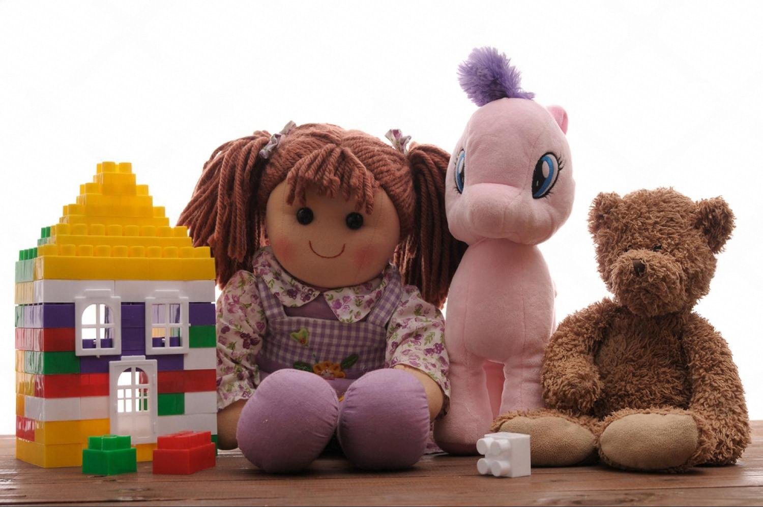Plastic construction kit house next to soft toys on a wooden floor